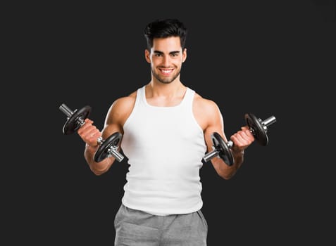 Portrait of handsome young man lifting weights, isolated over a gray background