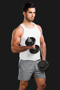 Portrait of handsome young man lifting weights, isolated over a gray background