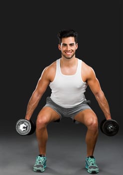 Portrait of handsome young man lifting weights, isolated over a gray background