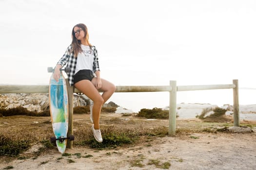 Beautiful and fashion young woman posing at the sunset with a skateboard