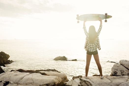 Beautiful and fashion young woman posing at the sunset with a skateboard