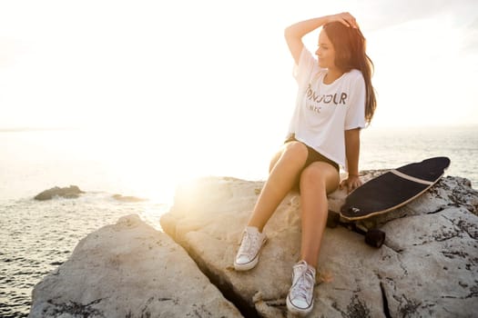 Beautiful and fashion young woman posing at the sunset with a skateboard