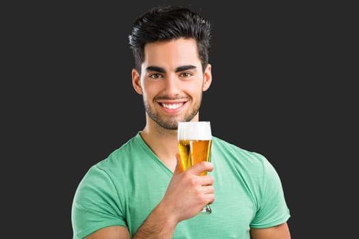Portrait of handsome young man tasting a draft beer, isolated on gray background