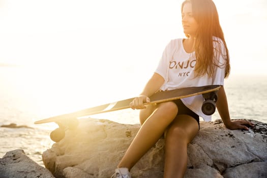 Beautiful and fashion young woman posing at the sunset with a skateboard