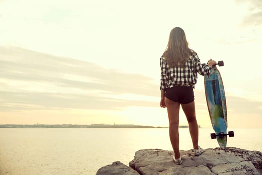 Beautiful and fashion young woman posing at the sunset with a skateboard