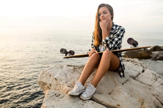 Beautiful and fashion young woman posing at the sunset with a skateboard