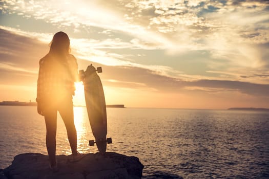 Beautiful and fashion young woman posing at the sunset with a skateboard