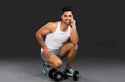 Portrait of handsome young man lifting weights, isolated over a gray background