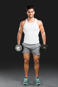 Portrait of handsome young man lifting weights, isolated over a gray background