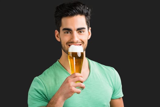 Portrait of handsome young man tasting a draft beer, isolated on gray background