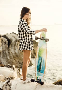 Beautiful and fashion young woman posing at the sunset with a skateboard