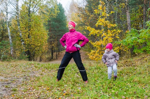 Woman with girl doing aerobics in the autumn park