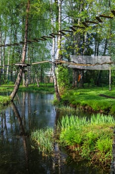 Dangerous ropeway with tether in rope park, trees with green leaves