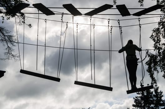 Silhouette of the girl on Dangerous ropeway with tether in rope park