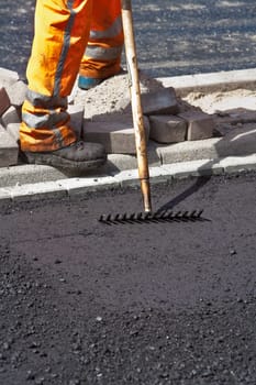 Manual worker resting after leveling new asphalt with a rake