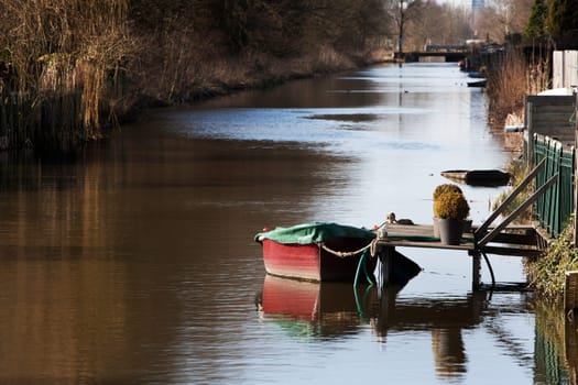 Tranquil and idyllic scene of a red boat with a green awning, moored with a rope, at a backyard jetty.