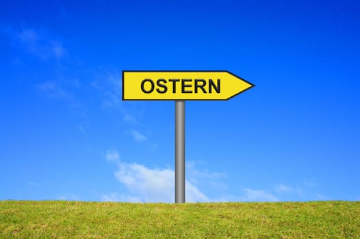 Yellow sign on a meadow in front of blue sky points towards Easter