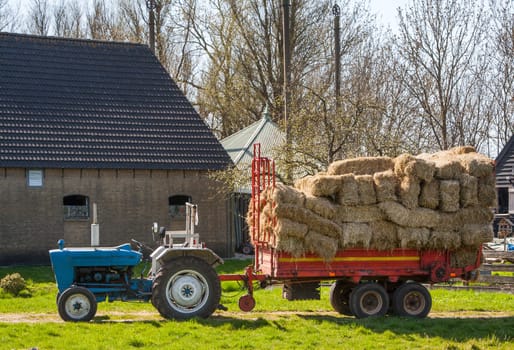Idyllic blue retro tractor with red hay wagon.  With the farm in the background.