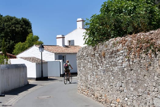 Picturesque street with white houses on Noirmoutier island, in France. And a stone wall on the right. The street is asphalted, which is nice for cyclists.