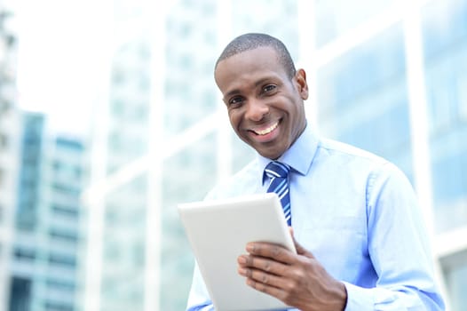 Smiling business man using tablet in front of office