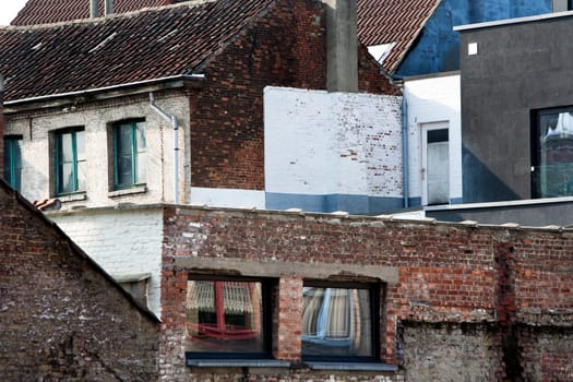 Residential neighborhood of brick houses built close together in Mechelen, Belgium. The windows (red and blue) at the other side of the street are reflected in the windows at the streetside. The bricks become an abstract picturesque community. Some walls are painted white, grey or black.