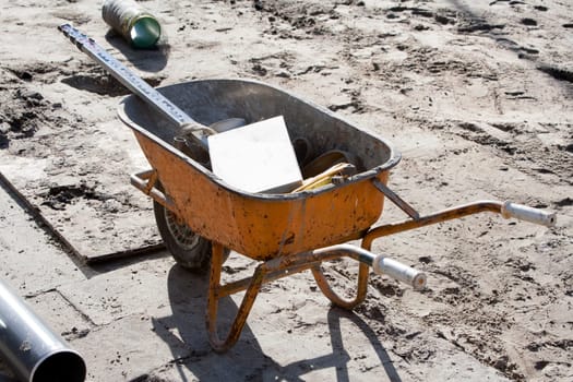 Orange wheelbarrow with tools on a construction site