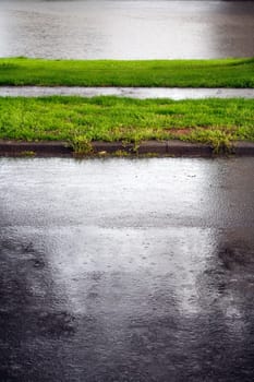It’s raining on the asphalt while sunlight is on the grass