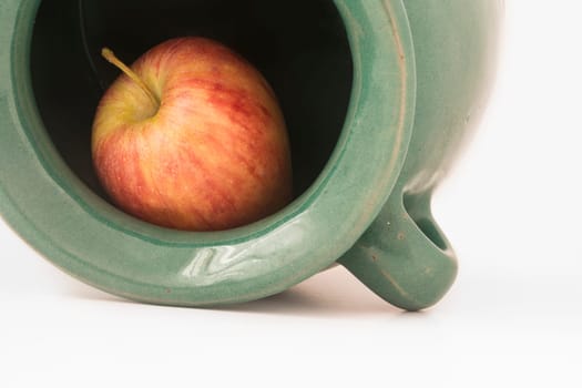 close up view of a red apple inside the greenish earthen jar isolated on white background.