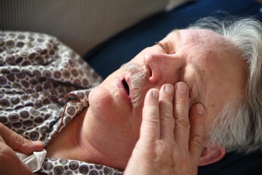 A senior man suffers the miseries of the flu while lying on a sofa.
