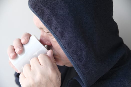 Older man wearing a black hoodie drinks his morning coffee.