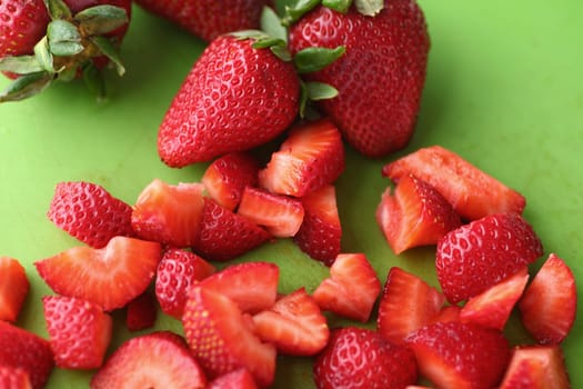 Fresh whole and chopped strawberries on a green cutting board