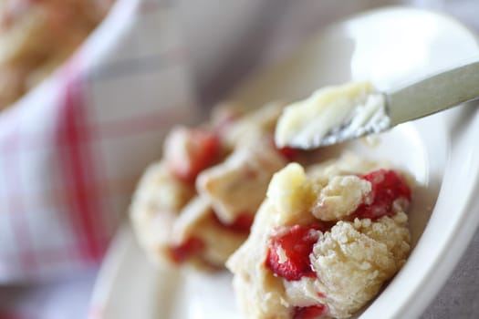 Spreading soft butter on a fresh-out-of-the-oven strawberry biscuit