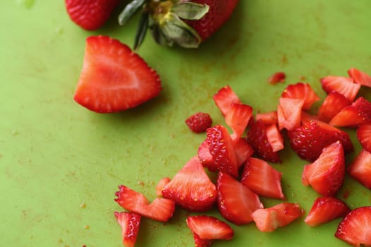 Fresh strawberries chopped, whole and half on a green cutting board
