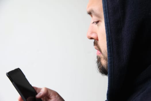 A young man wearing a black hoodie uses his cell phone.
