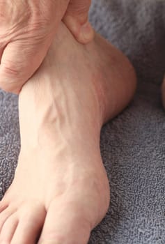 A man holds his foot near the ankle. Copy space included.