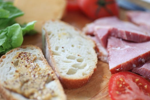 Bread with whole-grain mustard, ham slices, cheese, lettuce and tomato, ready to make into a lunch sandwich