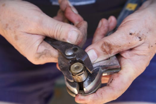 A man with muddy hands adjusts a bolt on a sprinkler head for a lawn.