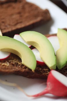 Avocado and radish slices on dark bread spread with whole grain mustard