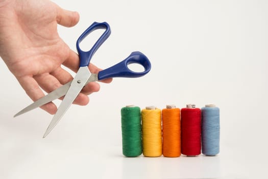 Multicolor Sewing Threads, Bobbins With A Hand Holding A Scissor Isolated on White Background.