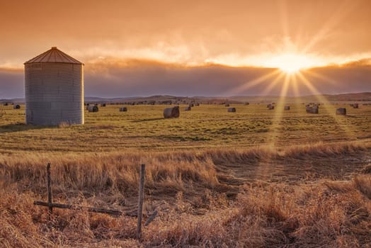 Landscape of the setting sun on the prairie with a grain elevator and sunburst.