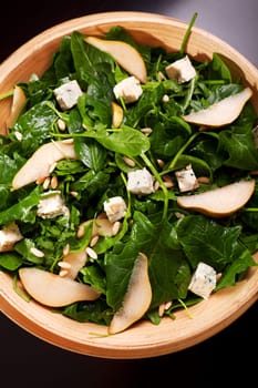 Fresh spinach salad with blue cheese, pears and honey served in a salad bowl, close up