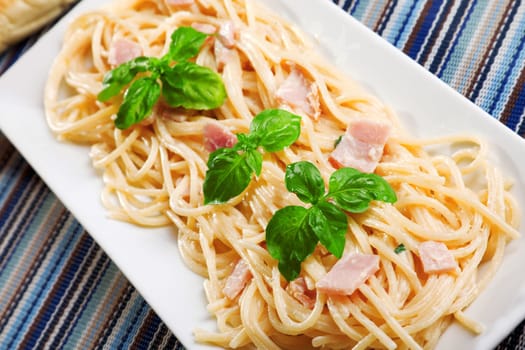 Spaghetti carbonara decorated with fresh basil leaves, close up