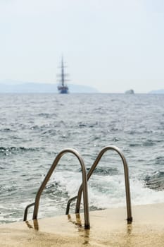 Bathing ladder on the rocky beach behind a sailing ship