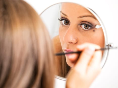 Applying make-up on young woman face, reflection in the mirror