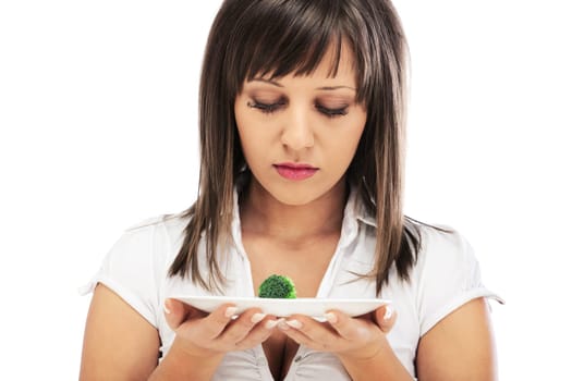 Young woman unhappy for eating healthy food, looking at small portion of raw broccoli, isolated on white background with copy space