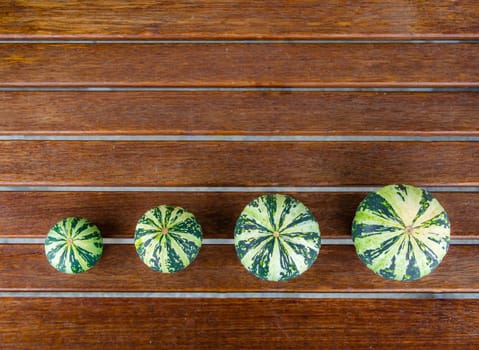 Still life with variety of green and yellow pumpkins cucurbita pepo spread on wooden table viewed from top, useable as seasonal autumn harvest Halloween housing decoration illustration
