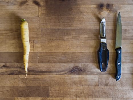 Yellow carrot, knife and peeler on a wooden board, meal preparation scene, cooking background