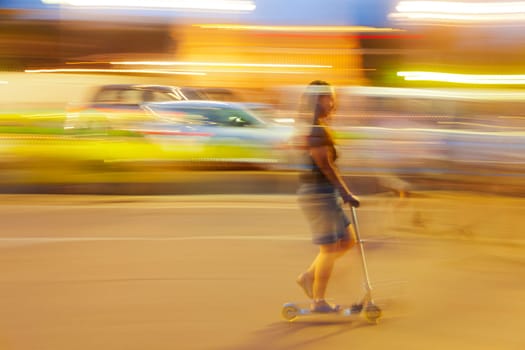 Young woman riding scooter at night in the center ot Nice, France