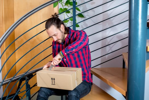 young man sitting in corridor and opening a package