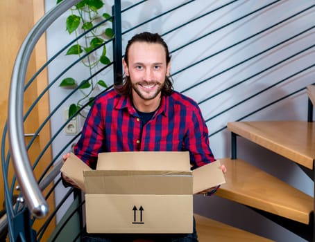 young man sitting in corridor and opening a package
